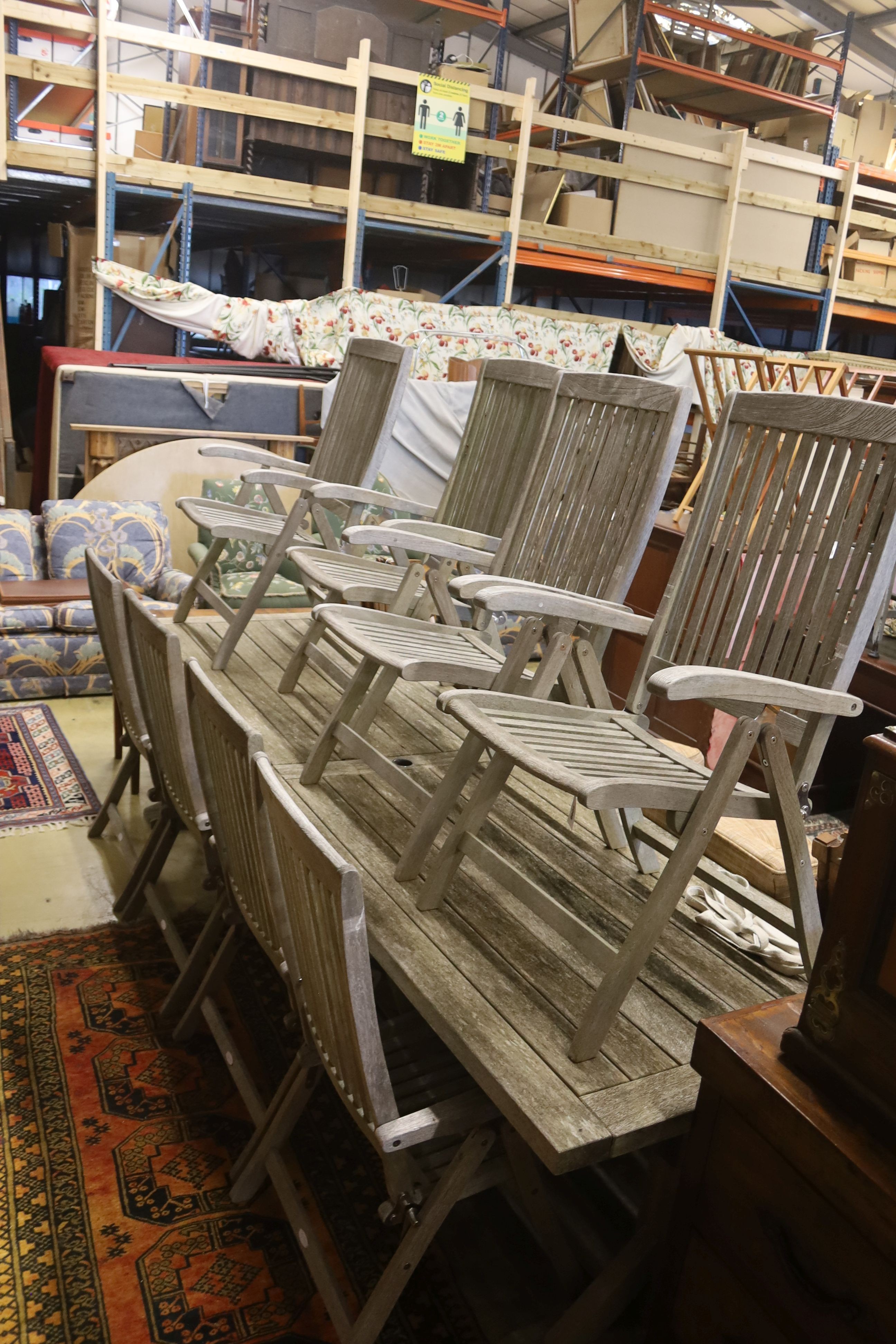 A suite of furniture comprising a weathered teak garden table, length 290cm, depth 90cm, height 74cm, and a set of eight Neptune teak folding garden armchairs